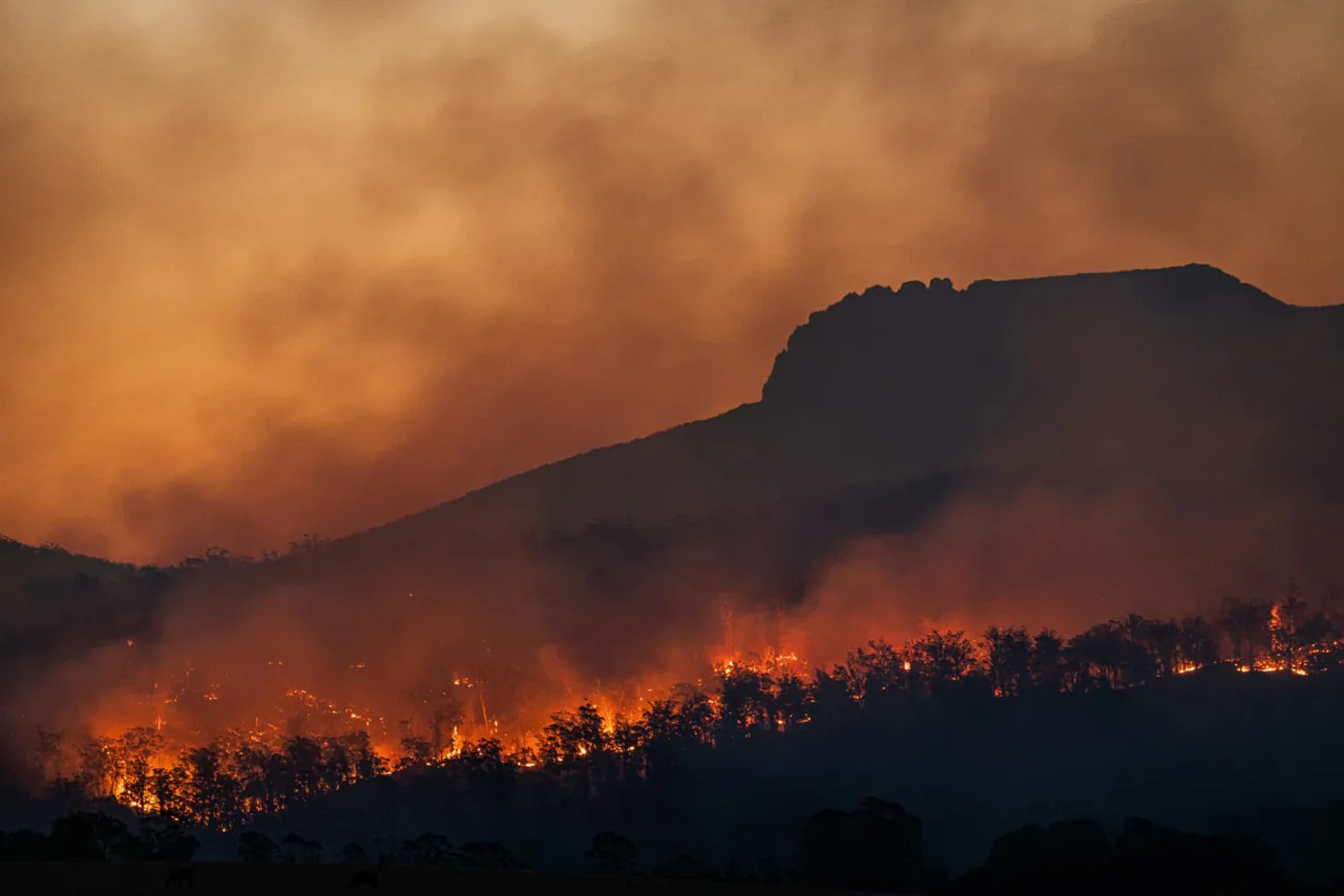 Wildfire burning along a ridgeline under heavy smoke at dusk